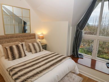 A bedroom with a bed and pillows next to a window with curtains at Yr Hen Ysgol The Old School in Prenteg