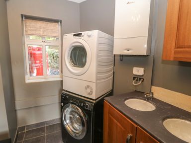 A laundry room with stacked washer and dryer next to a countertop with two sinks at Yr Hen Ysgol The Old School in Prenteg