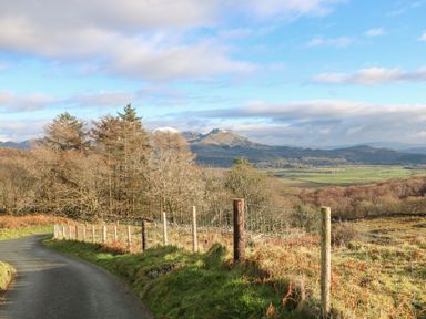 A countryside road bordered by a wire fence and trees with a mountain range in the background at Yr Hen Ysgol The Old School in Prenteg