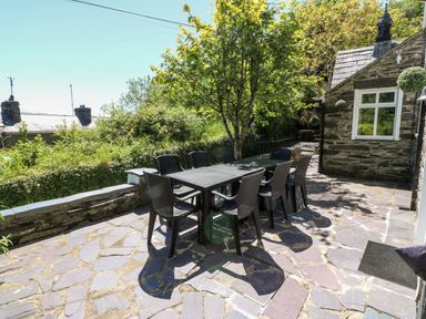An outdoor patio area with a table and eight chairs under a tree next to a stone building at Yr Hen Ysgol The Old School in Prenteg