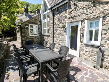 An outdoor patio area with a black table and eight black chairs next to a stone wall building at Yr Hen Ysgol The Old School in Prenteg