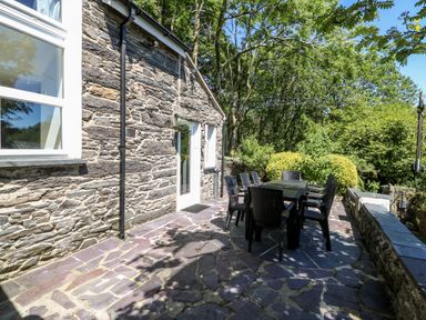 An outdoor stone patio with a table and chairs next to a stone building with windows and a door at Yr Hen Ysgol The Old School in Prenteg