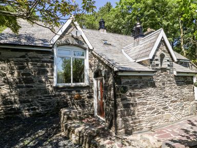 Stone exterior of a cottage with a wooden door and windows surrounded by trees at Yr Hen Ysgol The Old School in Prenteg