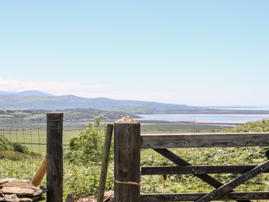A wooden gate and fence overlooking green fields and a body of water with hills in the background at Yr Hen Ysgol The Old School in Prenteg