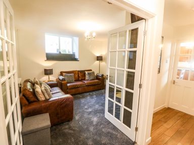A sitting room with two brown leather sofas two lamps a window and a carpet at Yr Hen Ysgol The Old School Prenteg