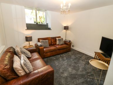 A living room with two brown leather sofas a floor lamp a table lamp a wall-mounted window a small round table and a television on a wooden stand at Yr Hen Ysgol The Old School in Prenteg