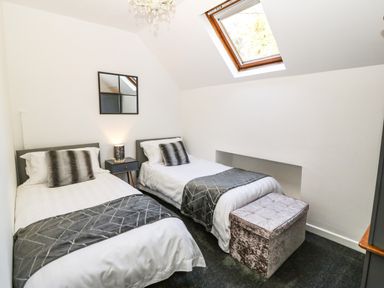 A bedroom with two single beds a bedside table with a lamp a mirror a skylight window and a storage bench at Yr Hen Ysgol The Old School in Prenteg