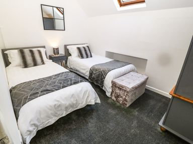A bedroom with two single beds a nightstand with a lamp a mirror a storage bench and a skylight at Yr Hen Ysgol The Old School in Prenteg