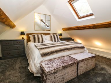 A bedroom with a bed two bedside tables with lamps a skylight and two storage ottomans at Yr Hen Ysgol The Old School in Prenteg
