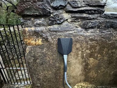 A stone wall with a black outdoor water tap and a metal gate on the left at Yr Hen Ysgol The Old School in Prenteg