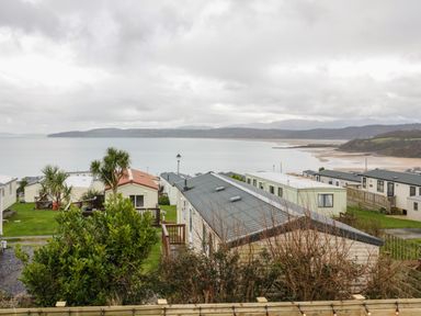 A coastal view with mobile homes trees and a beach at The Sandy Bee in Benllech