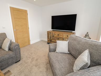 A living room with grey sofas a wooden tv cabinet and a flat screen tv at The Sandy Bee in Benllech
