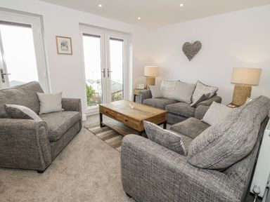 A living room with three gray sofas a wooden coffee table and two lamps at The Sandy Bee in Benllech