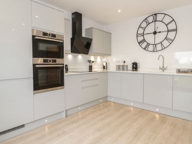 A kitchen with built in ovens a stovetop kettle sink utensils and a large wall clock at The Sandy Bee in Benllech