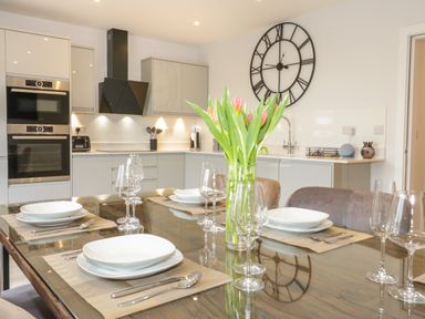 A kitchen with a dining table set with plates and glasses with tulips in a vase and a large wall clock at The Sandy Bee in Benllech