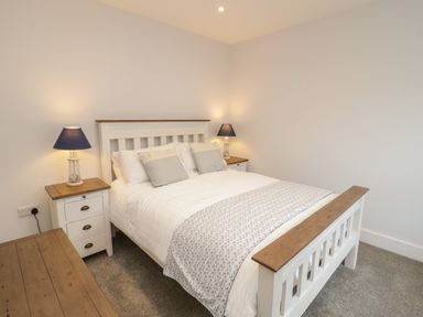 A bedroom with a white bed frame wooden top bedside cabinets with lamps and a dresser at The Sandy Bee in Benllech