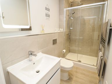 A bathroom with a sink a toilet a glass shower enclosure and a towel rack at The Sandy Bee in Benllech