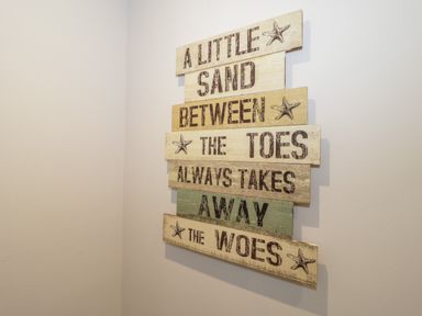 A wooden wall sign with text about sand and toes on a plain wall at The Sandy Bee in Benllech
