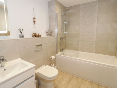A bathroom with a bathtub and shower, toilet, sink, and decorative items on a shelf at The Sandy Bee in Benllech