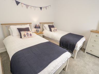 A bedroom with two single beds, a nightstand with a lamp, and a dresser at The Sandy Bee in Benllech