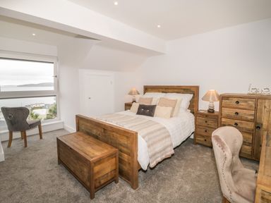 A bedroom with a wooden bed and chest at the foot a window with a chair and wooden furniture at The Sandy Bee in Benllech