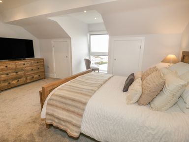 A bedroom with a wooden bed and dresser a chair near a window and a lamp at The Sandy Bee in Benllech