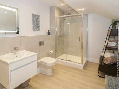 A bathroom with a sink, toilet, glass shower enclosure, and shelving unit with towels at The Sandy Bee in Benllech