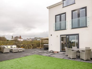 An outdoor patio area with seating and dining furniture next to a modern house at The Sandy Bee in Benllech