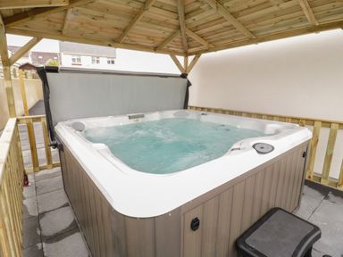 An outdoor hot tub with water jets under a wooden gazebo at The Sandy Bee in Benllech