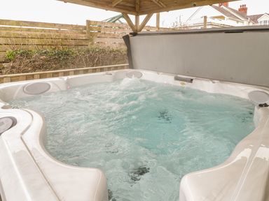 A bubbling outdoor hot tub under a wooden roof with a fenced garden and houses in the background