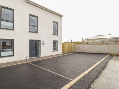 A modern building with a black front door and several windows next to an empty paved parking area at The Sandy Bee in Benllech