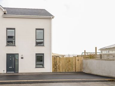 A beige two-story house with dark framed windows and a dark door next to a wooden fence at The Sandy Bee in Benllech