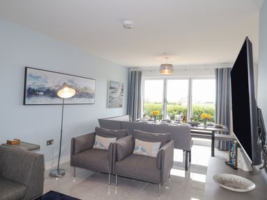 A living room with two armchairs a floor lamp paintings a dining table set and a television at Chandlers Retreat in Newport Pembrokeshire