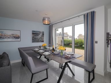 A dining area with a table set for six with yellow flowers next to glass doors at Chandlers Retreat in Newport Pembrokeshire