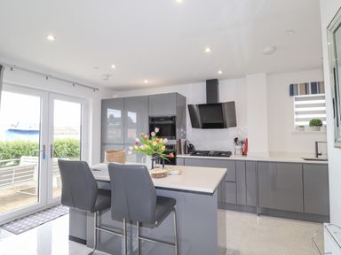 A kitchen with grey cabinets a kitchen island with two chairs and flowers on it at Chandlers Retreat in Newport Pembrokeshire