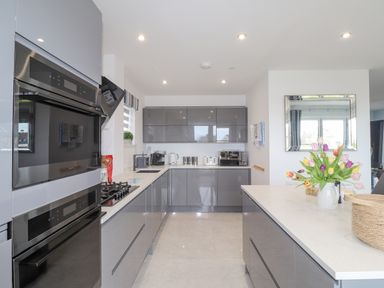 A modern kitchen with grey cabinets a white countertop flowers in a vase and built in ovens at Chandlers Retreat in Newport Pembrokeshire