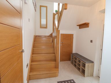 A hallway with wooden stairs a shoe rack bench a coat rack and a mirror at Chandlers Retreat in Newport Pembrokeshire