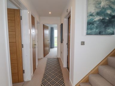 A hallway with wooden doors a patterned runner rug a staircase and a painting on the wall at Chandlers Retreat in Newport Pembrokeshire
