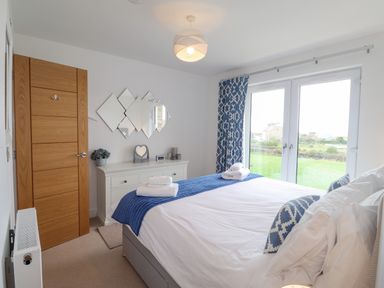 A bedroom with a bed pillows towels dresser and a door with windows overlooking a lawn at Chandlers Retreat in Newport Pembrokeshire