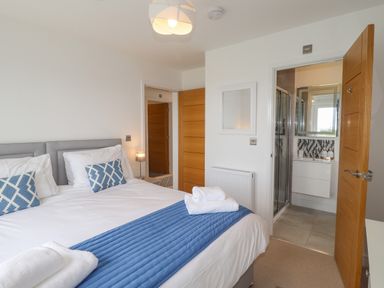 A bedroom with a double bed with blue runner and pillows and an open doorway leading to a bathroom at Chandlers Retreat in Newport Pembrokeshire