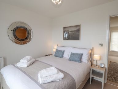 A bedroom with a double bed white bedding two blue patterned pillows towels on bed a bedside table with a lamp and a small clock a circular decorative mirror on the wall a framed photo above the bed at Chandlers Retreat Newport Pembrokeshire