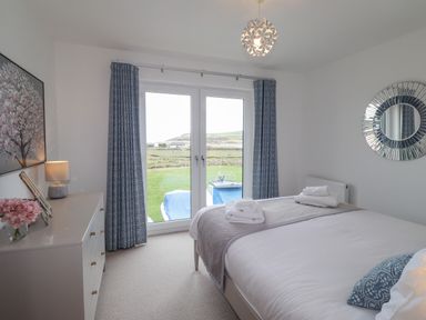 A bedroom with a bed towel set by patio doors and a dresser with a lamp and flowers at Chandlers Retreat in Newport Pembrokeshire
