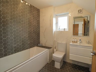 A bathroom with a bathtub a toilet a sink with cabinet a mirror and a window at Chandlers Retreat Newport Pembrokeshire
