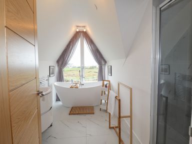 A bathroom with a freestanding bathtub near a large window with curtains wooden towel rack and a shower at Chandlers Retreat in Newport Pembrokeshire