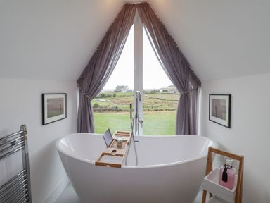A bathroom with a freestanding bathtub facing a large window with curtains at Chandlers Retreat in Newport Pembrokeshire