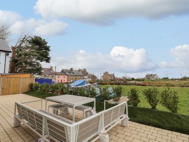 An outdoor patio with a table and benches overlooking a grassy field and houses at Chandlers Retreat in Newport Pembrokeshire
