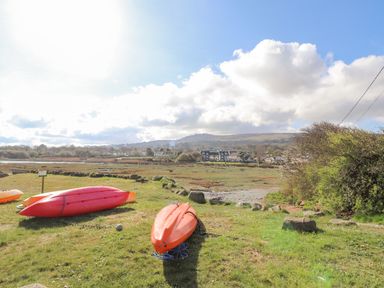 Kayaks on grass near water with houses and hills in the background at Chandlers Retreat in Newport Pembrokeshire