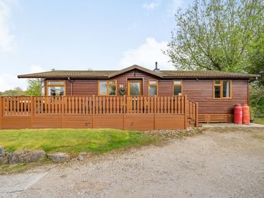 A wooden cabin with a fenced porch and propane tanks outside at Lakeview Lodge in South Lakeland Leisure Village