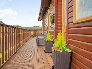 A wooden balcony with railing two planters flowers and a bench at Lakeview Lodge in South Lakeland Leisure Village