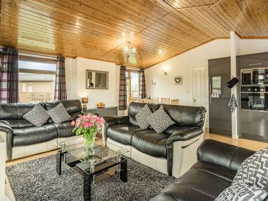 A living room with black and white sofas a glass coffee table with flowers a dining table and kitchen cabinets at Lakeview Lodge in South Lakeland Leisure Village